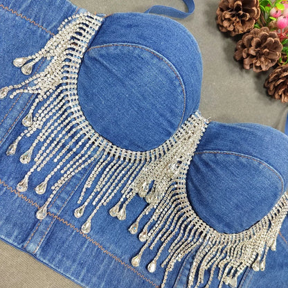 A denim corset with hanging rhinestones strikes a bold balance between rugged edge and high-glam allure. The structured denim hugs the body, giving it that classic, sculpted silhouette, while the cascading rhinestones add mov